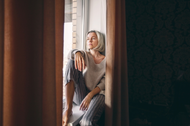 A woman sitting on a window sill feeling sad.