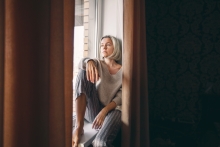 A woman sitting on a window sill feeling sad.